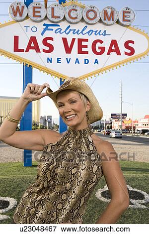 Stock Photo - Mid-adult woman wearing cowboy hat in front of Welcome to Las Vegas sign, portrait. Fotosearch
