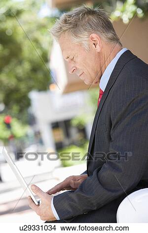 Middle-aged businessman using laptop outdoor View Large Photo Image Picture - Middle-aged businessman using laptop outdoor. Fotosearch