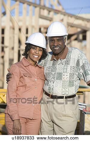Stock Image - Middle-aged couple at construction site, portrait. Fotosearch
