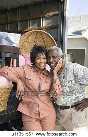 Stock Photo - Middle-aged couple in front of lorry with furniture. Fotosearch