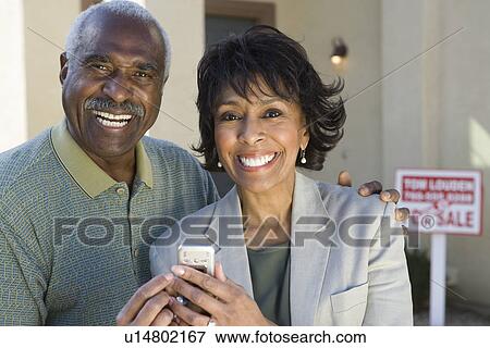 Stock Photo - Middle-aged couple in front of new home. Fotosearch