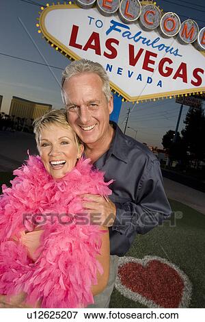 Stock Photo - Middle-aged couple in front of Welcome to Las Vegas sign, portrait. Fotosearch