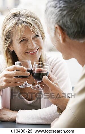 Stock Image - Middle-aged couple sitting at outdoor cafe in Rome toasting wine glasses, close up. Fotosearch