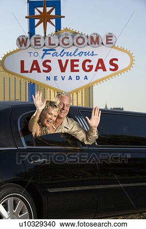 Stock Image - Middle-aged couple sitting in limousine and waving in front of Welcome to Las Vegas sign. Fotosearch