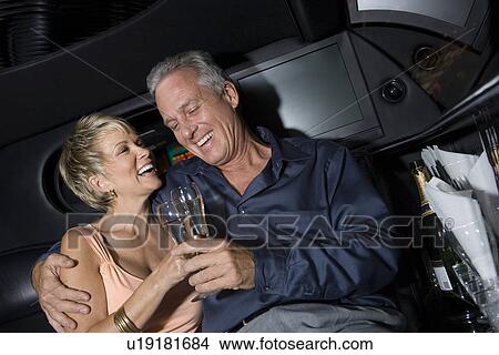 Picture - Middle-aged couple sitting on back seat of limousine and drinking champagne. Fotosearch