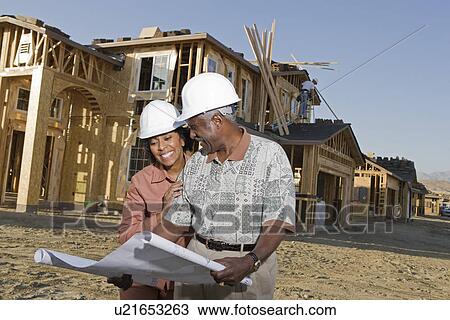 Middle-aged couple watching blueprints at construction site View Large Photo Image Stock Image - Middle-aged couple watching blueprints at construction site. Fotosearch