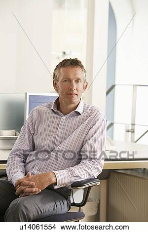 Picture - Middle-aged male office worker sitting in cubicle, portrait. Fotosearch