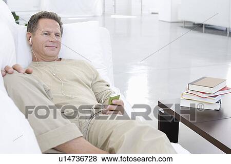 Stock Photo - Middle-aged man listening to music on sofa. Fotosearch