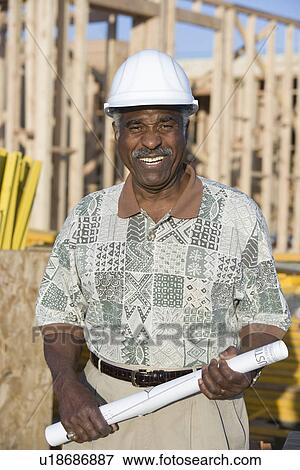 Middle-aged man with blueprints, construction site View Large Photo Image Stock Photo - Middle-aged man with blueprints, construction site. Fotosearch
