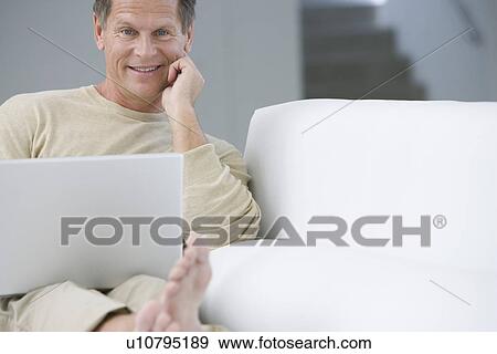 Stock Photo - Middle-aged man with laptop on sofa. Fotosearch