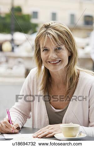Stock Image - Middle-aged woman at outdoor cafe in Rome writing postcards, portrait. Fotosearch