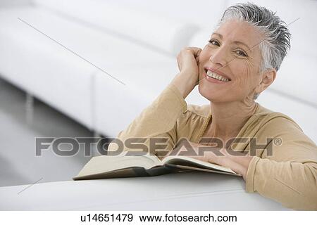 Middle-aged woman reading book on sofa View Large Photo Image Stock Photo - Middle-aged woman reading book on sofa. Fotosearch