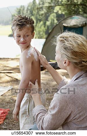 Stock Photo - Mother Applying Suntan Lotion on Son (7-9) at campsite.. Fotosearch