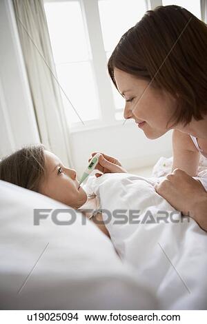 Mother checking temperature of daughter in bed View Large Photo Image Picture - Mother checking temperature of daughter in bed. Fotosearch