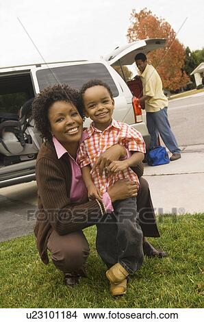 Mother embracing young son by car, father unloading baggage View Large Photo Image Picture - Mother embracing young son by car, father unloading baggage. Fotosearch