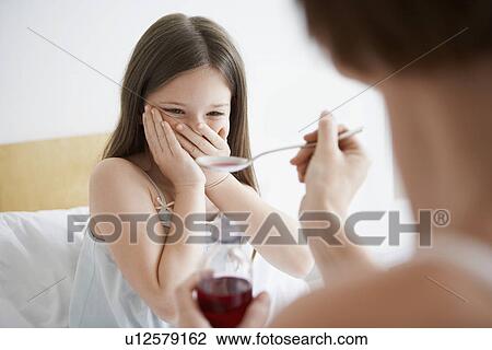 Mother giving cough syrup to reluctant daughter in bedroom View Large Photo Image Stock Image - Mother giving cough syrup to reluctant daughter in bedroom. Fotosearch