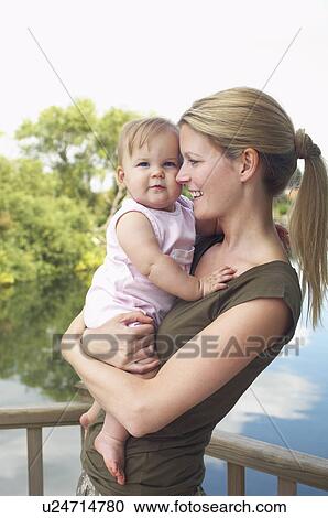 Stock Image - Mother holding daughter by lake, half length. Fotosearch