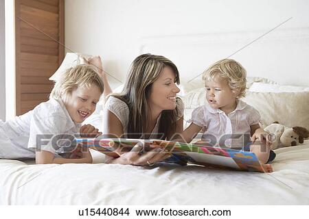 Picture - Mother lying on stomach on bed, Playing with Sons. Fotosearch