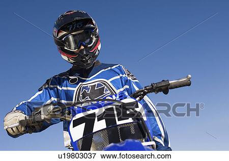 Motocross racer on bike against blue sky, (low angle view) View Large Photo Image Stock Photo - Motocross racer on bike against blue sky, (low angle view). Fotosearch
