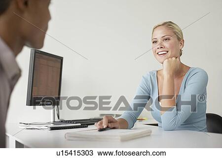 Stock Image - Office worker and client sitting at desk, side view. Fotosearch
