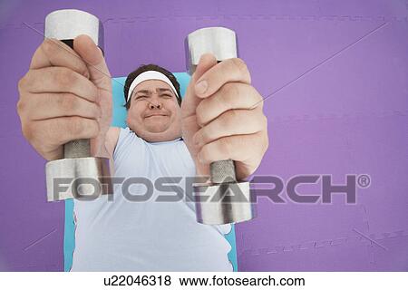 Stock Photo - Overweight Man lying down Lifting dumbbells, overhead view. Fotosearch