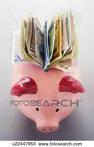 Stock Image - Paper money coming out of piggy bank, view from above. Fotosearch