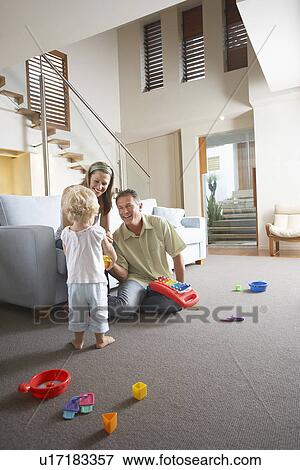 Stock Photo - Parents sitting in living room, watching son Playing with toys. Fotosearch