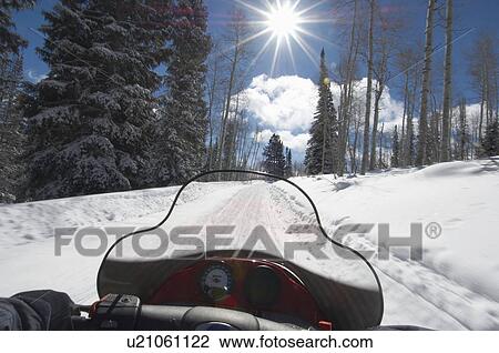 Stock Image - Person driving snowmobile through snow, personal perspective. Fotosearch