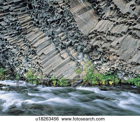 Stock Photograph - Plants and river at base of columnar basalt cliff. Fotosearch