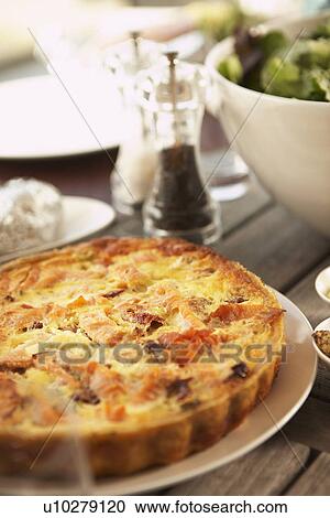 Stock Image - Plate of Quiche setting on picnic table among other dishes. Fotosearch
