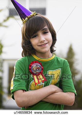 Picture - Portrait of boy (10-12) in party hat smiling, arms crossed. Fotosearch