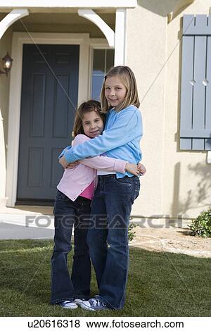 Stock Photo - Portrait of girls (609) hugging in front of house. Fotosearch