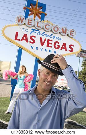 Portrait of mid-adult man in front of Welcome to Las Vegas sign, mid-adult woman in background. View Large Photo Image Stock Image - Portrait of mid-adult man in front of Welcome to Las Vegas sign, mid-adult woman in background.. Fotosearch