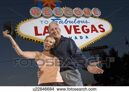 Picture - Portrait of middle-aged couple in front of Welcome to Las Vegas sign, low angle view. Fotosearch