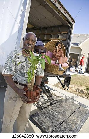 Stock Image - Portrait of middle-aged man with potted plant, woman in background, outdoors. Fotosearch