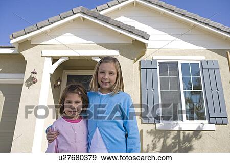 Stock Photo - Portrait of sisters (6-9) in front of house. Fotosearch