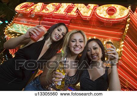 Stock Image - Portrait of three young women toasting in front of illuminated casino, Las Vegas, Nevada, USA. Fotosearch