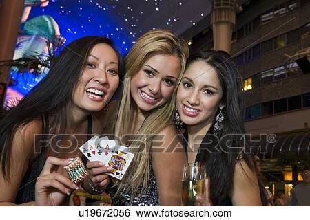 Stock Photograph - Portrait of three young women with playing cards, gambling chips and champagne in front of casino, Las Vegas, Nevada, USA. Fotosearch
