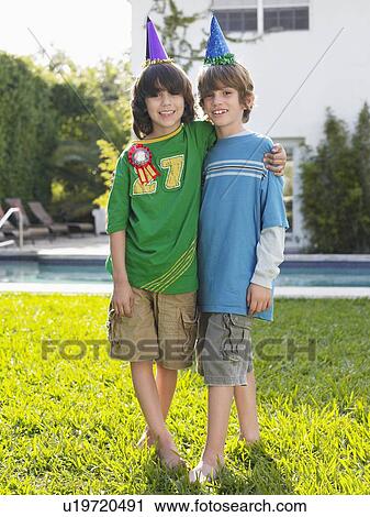 Stock Image - Portrait of two boys (10-12) in party hats in yard. Fotosearch
