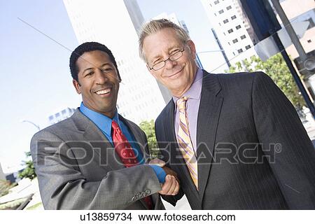Picture - Portrait of two businessmen shaking hands, outdoors. Fotosearch