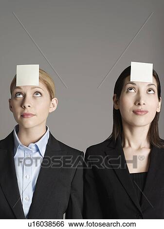 Stock Photograph - Portrait of two female office workers with sticky notes on forehead. Fotosearch