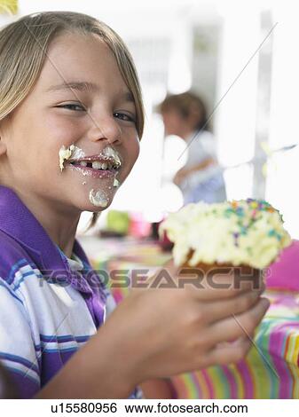 Stock Photograph - Portrait of young boy (7-9) eating cupcake. Fotosearch