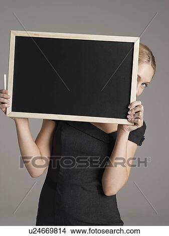 Picture - Portrait of young female teacher peeking from behind blackboard. Fotosearch