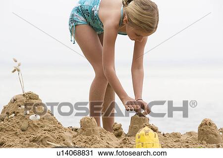 Stock Image - Pre-teen girl building sand castle on beach. Fotosearch