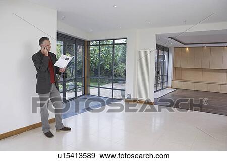 Stock Photo - Real estate agent using mobile phone in new property. Fotosearch