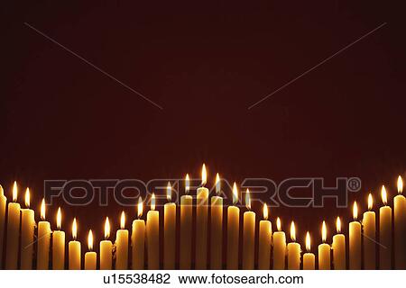 Stock Image - Row of lit candles, on black background. Fotosearch