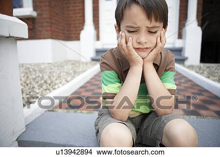Picture - Sad little boy sitting on front steps of house, close up. Fotosearch