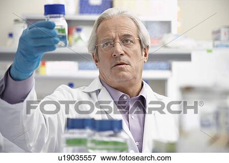 Stock Photo - Scientist looking at specimen bottle in laboratory. Fotosearch