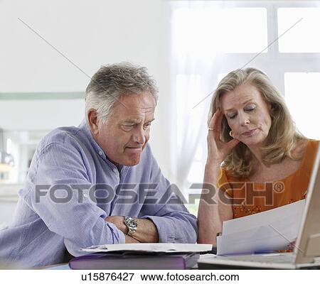 Senior couple looking at bills, sitting at dining table View Large Photo Image Stock Photo - Senior couple looking at bills, sitting at dining table. Fotosearch