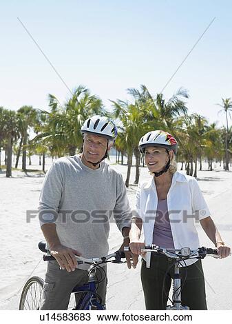 Stock Image - Senior couple on bicycles on tropical beach. Fotosearch